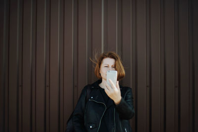 Portrait of young woman drinking against wall