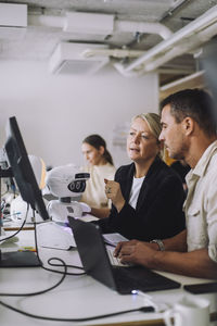 Female mature professor explaining phd student over computer in innovation lab