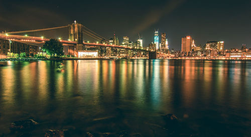 Illuminated bridge over river in city against sky at night