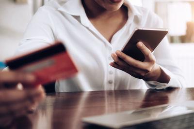 Midsection of businesswoman making mobile payment while sitting at desk in office