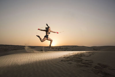 Young woman jumping on sand against sky