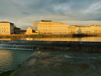 Buildings by river against sky in city