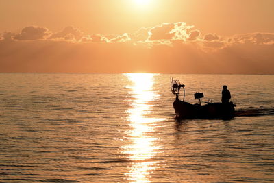 Silhouette people on sea against sky during sunset