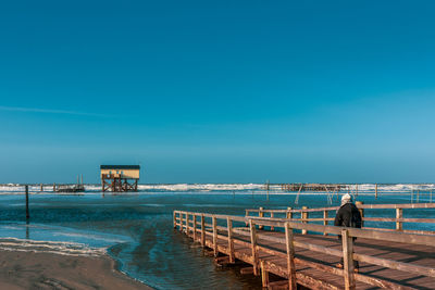 Pier over sea against clear blue sky