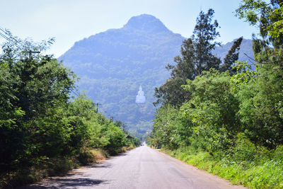 Road amidst trees and mountains against sky