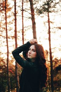 Portrait of young woman standing by tree in forest