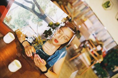 High angle view of young woman using smart phone sitting in restaurant seen through window