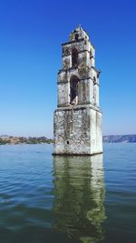 Old building by sea against clear blue sky