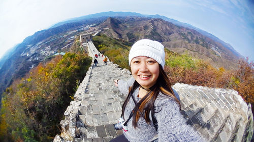 Fish-eye lens portrait of smiling woman against mountain range