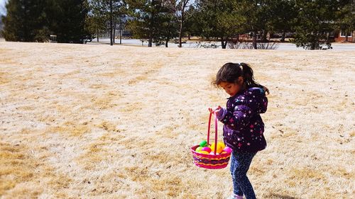 Side view of girl holding basket with easter eggs on field