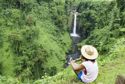 Male tourist with sun hat, looking at exotic fuipsia waterfall