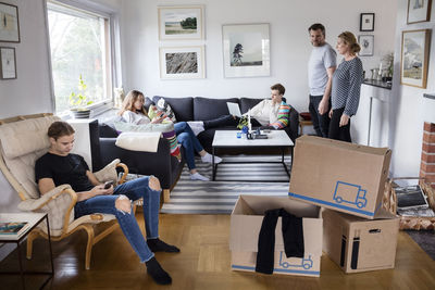 Parents looking at siblings sitting in living room with cardboard boxes