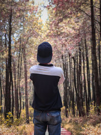 Rear view of man standing by trees in forest