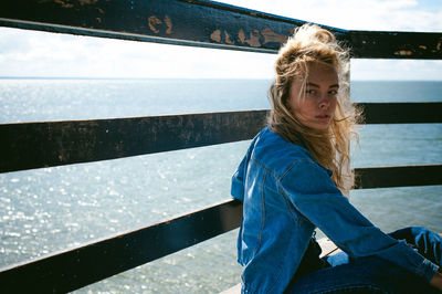 Young woman sitting on pier over sea against sky