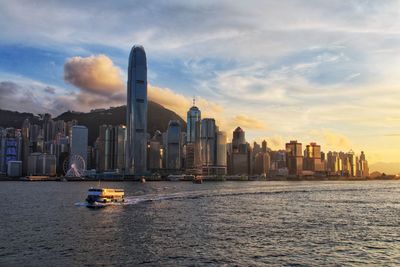 Sea by modern buildings against sky during sunset