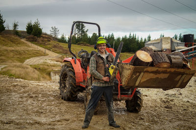 Portrait of worker holding chainsaw while standing at construction site