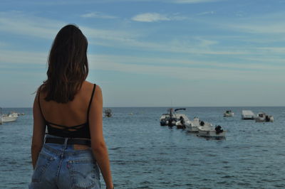 Rear view of friends standing at sea shore against sky
