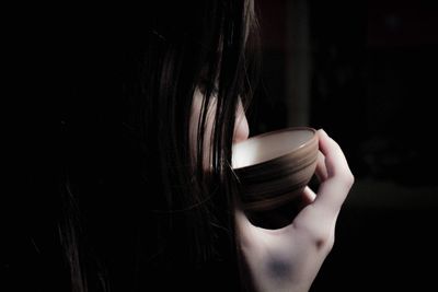 Close-up of woman drinking coffee against black background