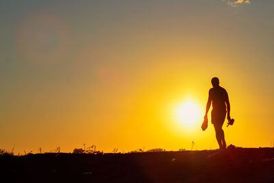 Silhouette man standing on land against sky during sunset