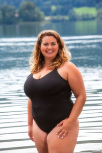 Portrait of smiling young woman standing against lake