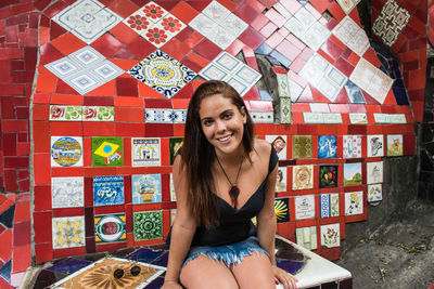 Portrait of smiling young woman sitting against wall