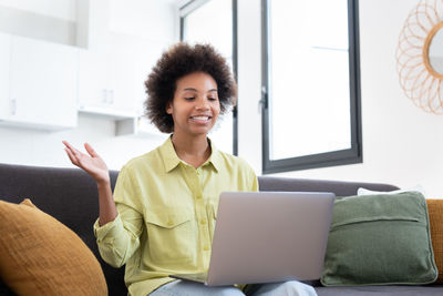 Young woman using laptop while sitting on sofa at home