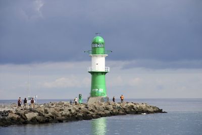 People and lighthouse by sea against sky
