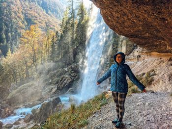 Full length of woman standing on rock against waterfall