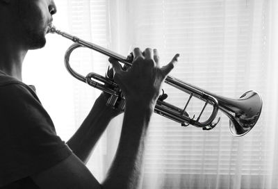 Midsection of young man playing trumpet while standing at home