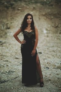 Portrait of beautiful young model standing in black evening gown on field