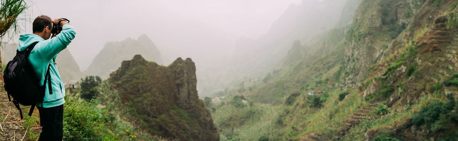 Side view of mid adult man photographing on mountain during foggy weather