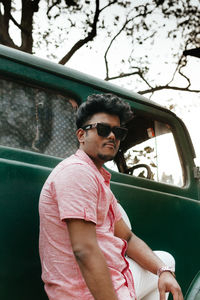 Young man looking away while standing by car