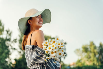 Smiling woman standing by flowering plants against sky