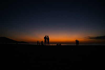 Silhouette people on beach against sky during sunset