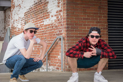 Full length of young man sitting on brick wall