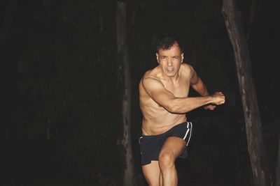 Portrait of shirtless man running against trees