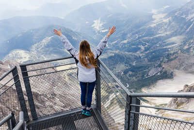 Woman standing by railing with mountains in background