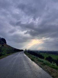 Road passing through land against cloudy sky