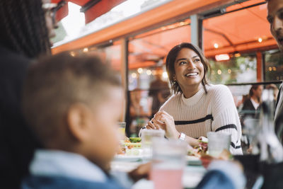 Smiling woman looking away while having food with family at restaurant