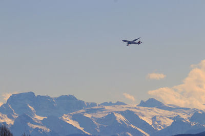 Low angle view of airplane flying over snowcapped mountains against sky