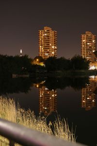 Illuminated buildings by lake against sky at night