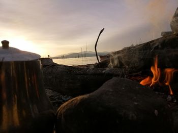 Close-up of bonfire on shore against sky during sunset