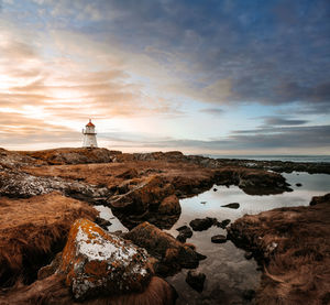 Lighthouse by sea against sky during sunset