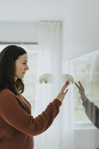 Mature woman touching smart tv mounted on wall at home