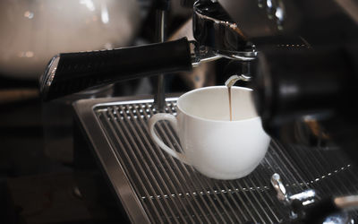 Close-up of coffee maker pouring drink in cup at cafe