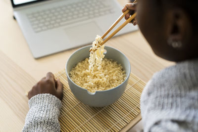 Young woman holding noddles in chopsticks while sitting at home