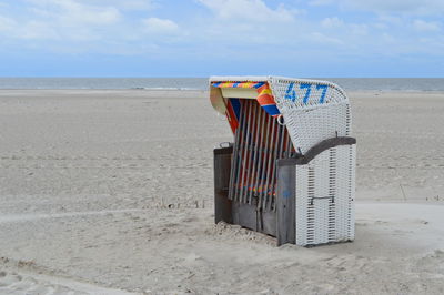 Hooded chair at beach against sky