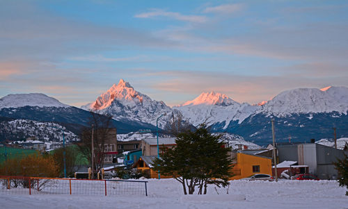 Houses on snow covered field by buildings against sky