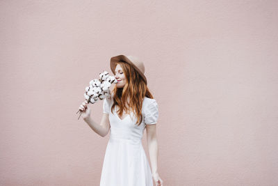 Woman holding white flower standing against wall