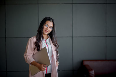 Portrait of young woman standing against wall